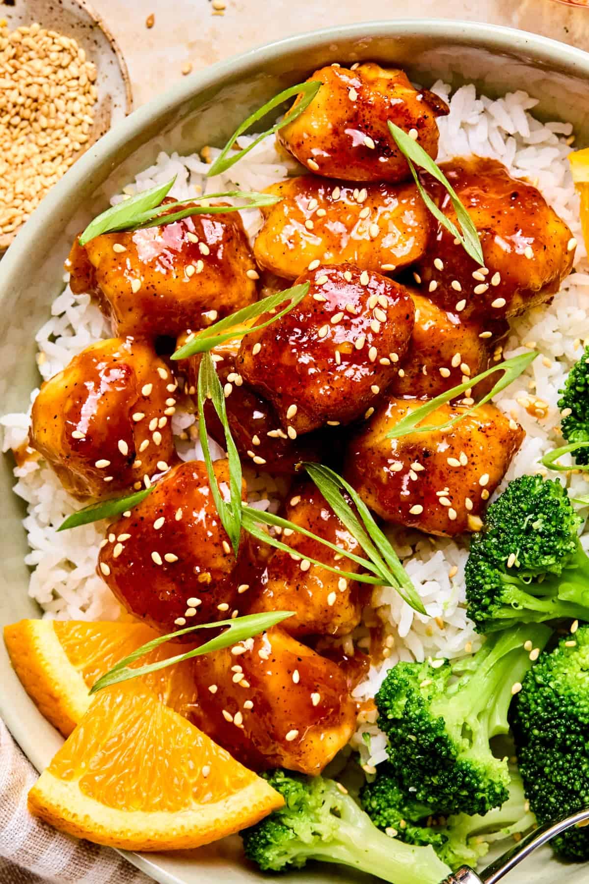 Orange chicken over rice topped with scallions and sesame seeds.