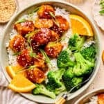 Spicy orange chicken over rice with broccoli and orange slices.