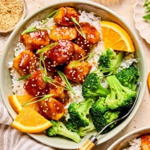 Spicy orange chicken over rice with broccoli and orange slices.