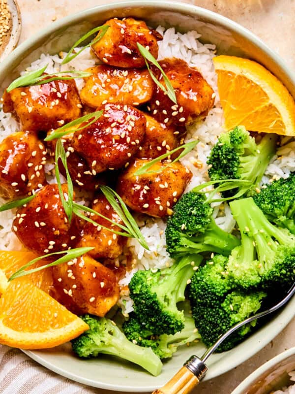 Spicy orange chicken over rice with broccoli and orange slices.