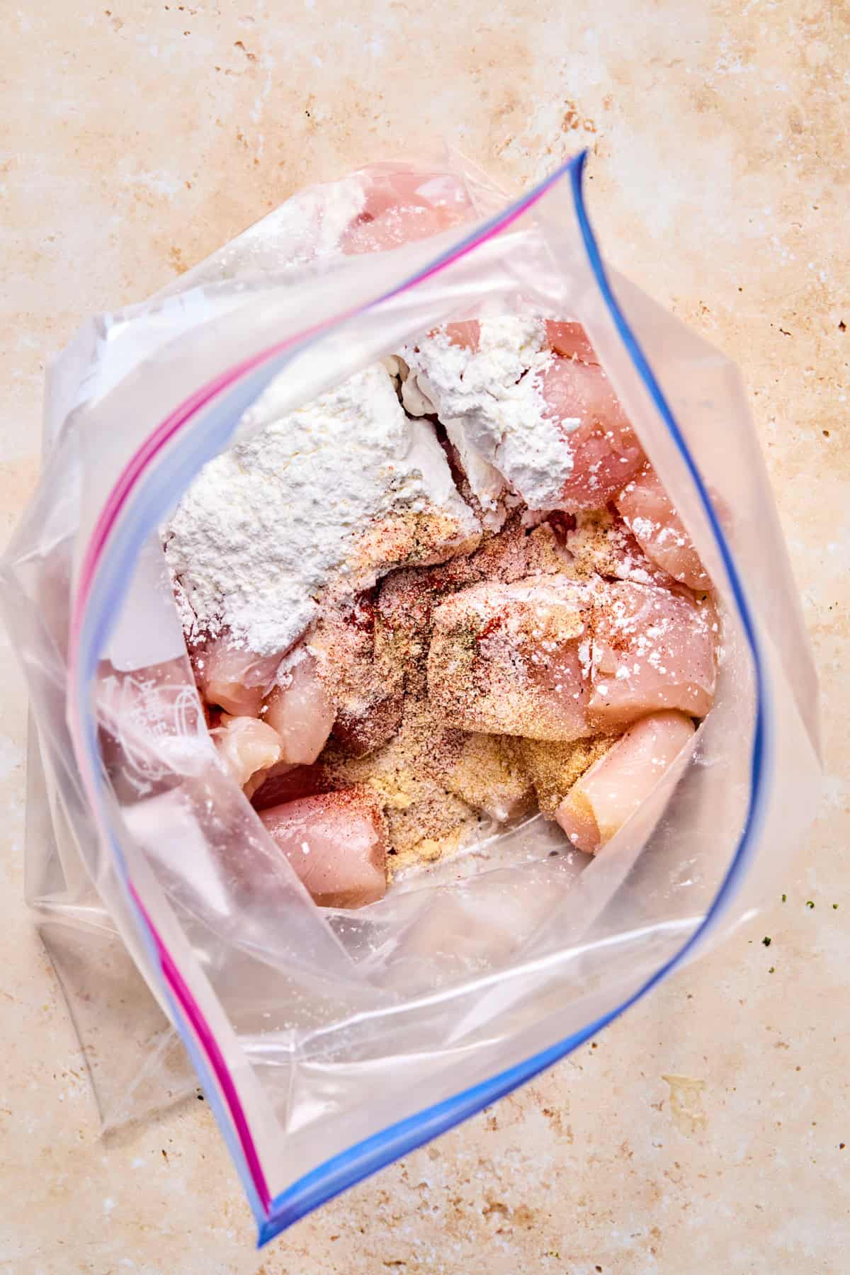 Plastic bag with cut up chicken pieces with cornstarch and seasoning.