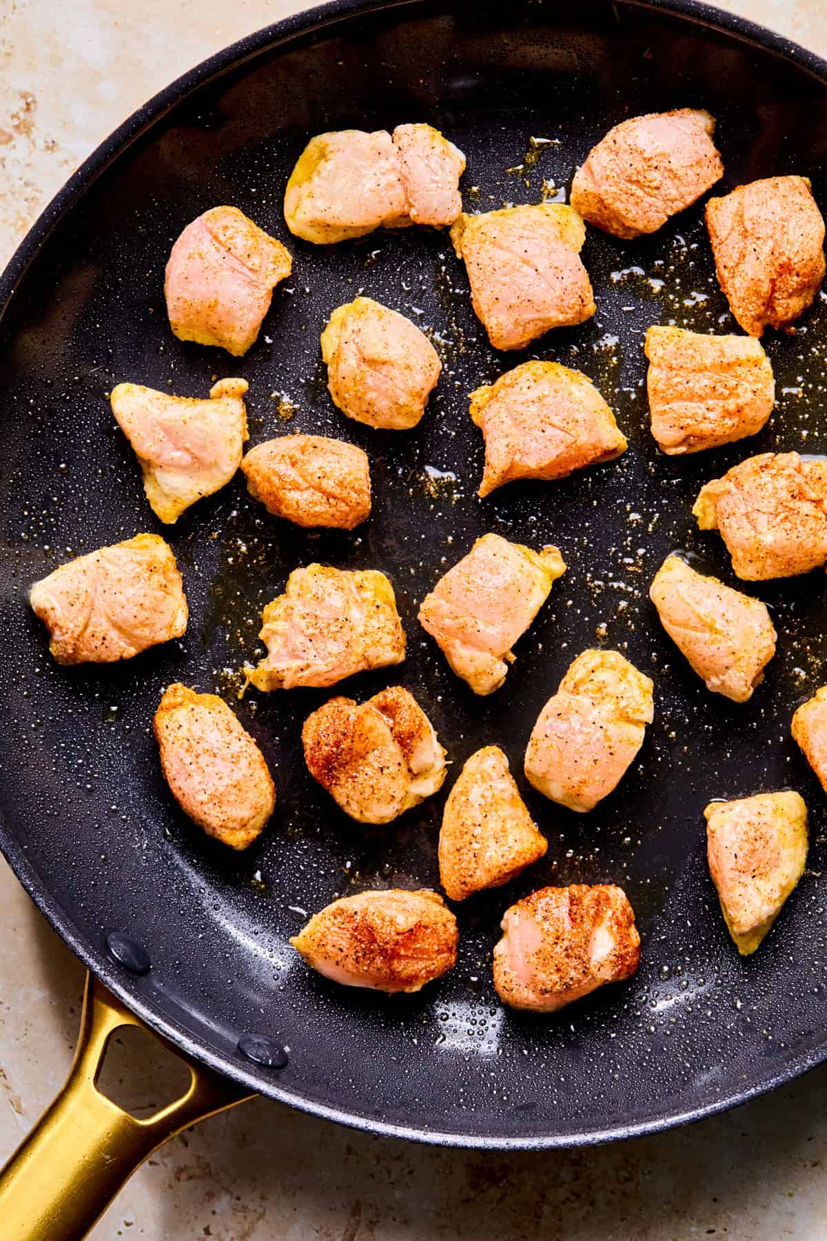 Chicken pieces searing in skillet.