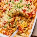 Casserole dish with baked cheesy tortellini with serving spoon scooping into it.