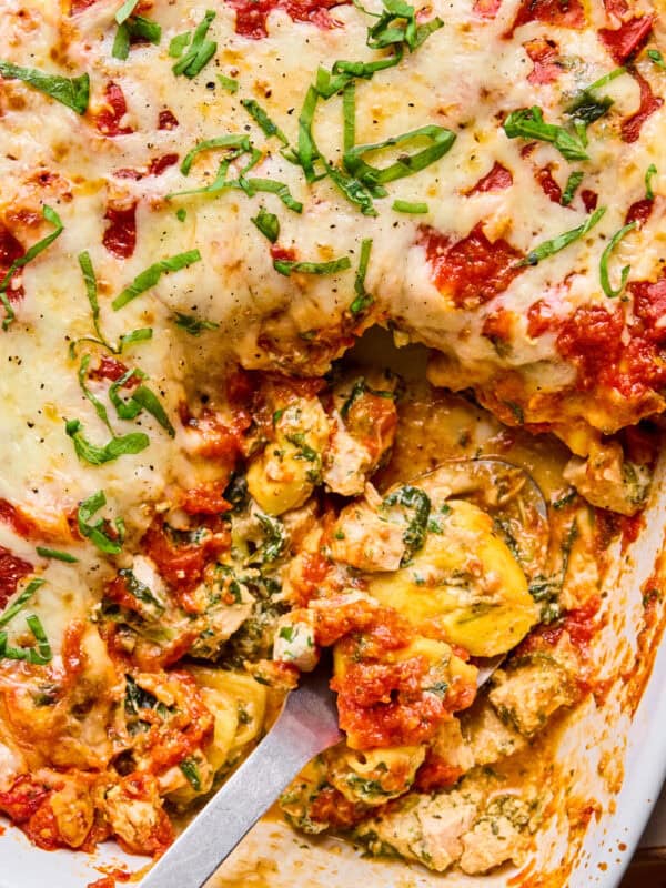 Casserole dish with baked cheesy tortellini with serving spoon scooping into it.