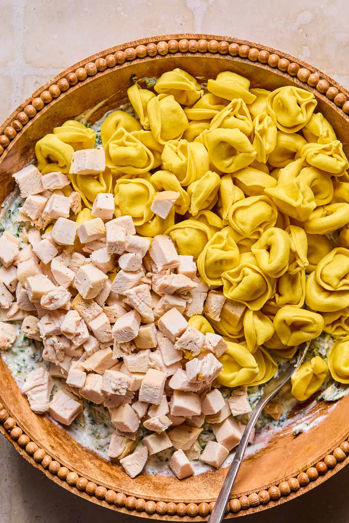 Tortellini and cubed chicken in mixing bowl with cheese mixture.