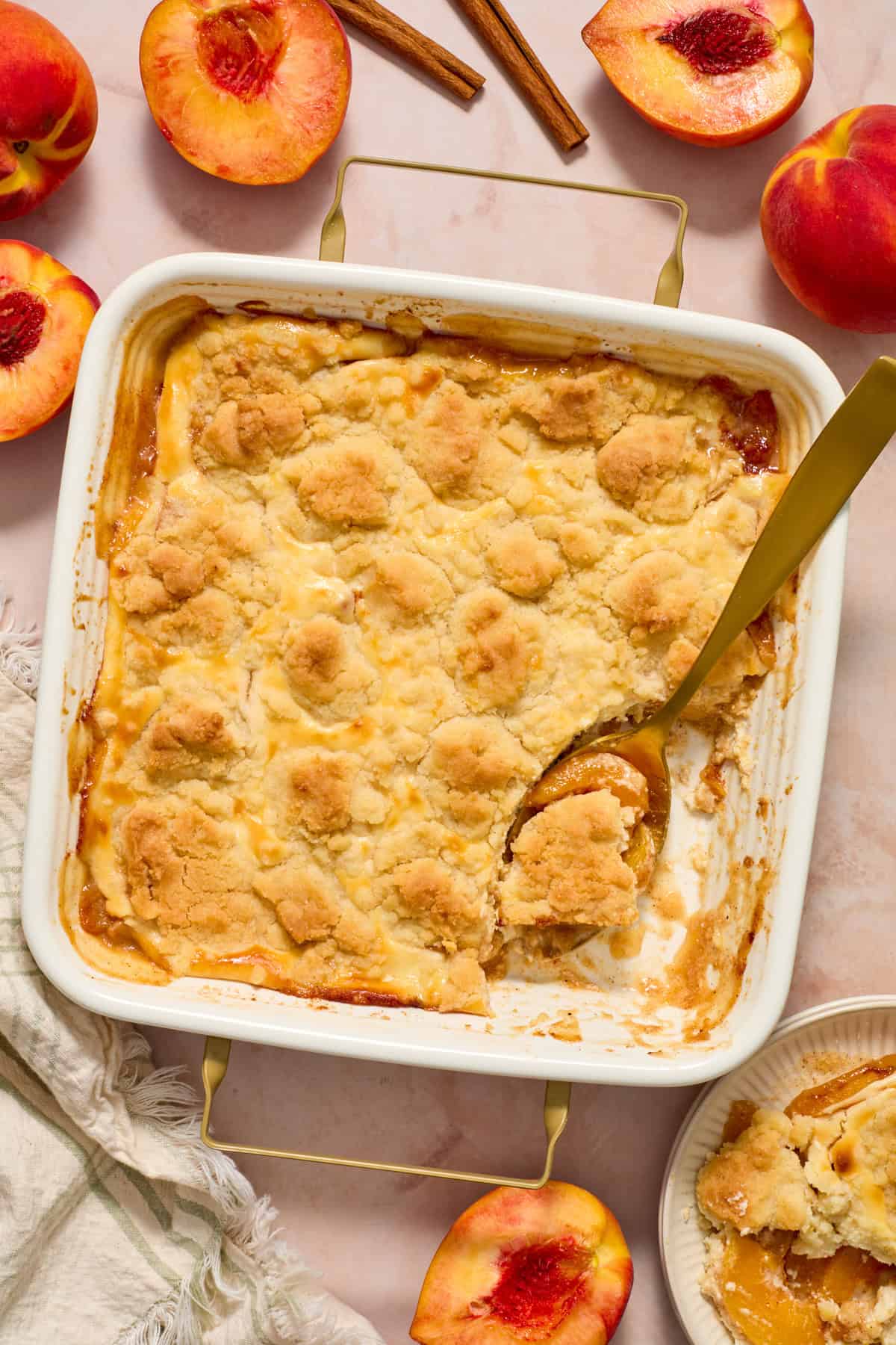 Peach cobbler cheesecake dessert in pan with serving spoon.