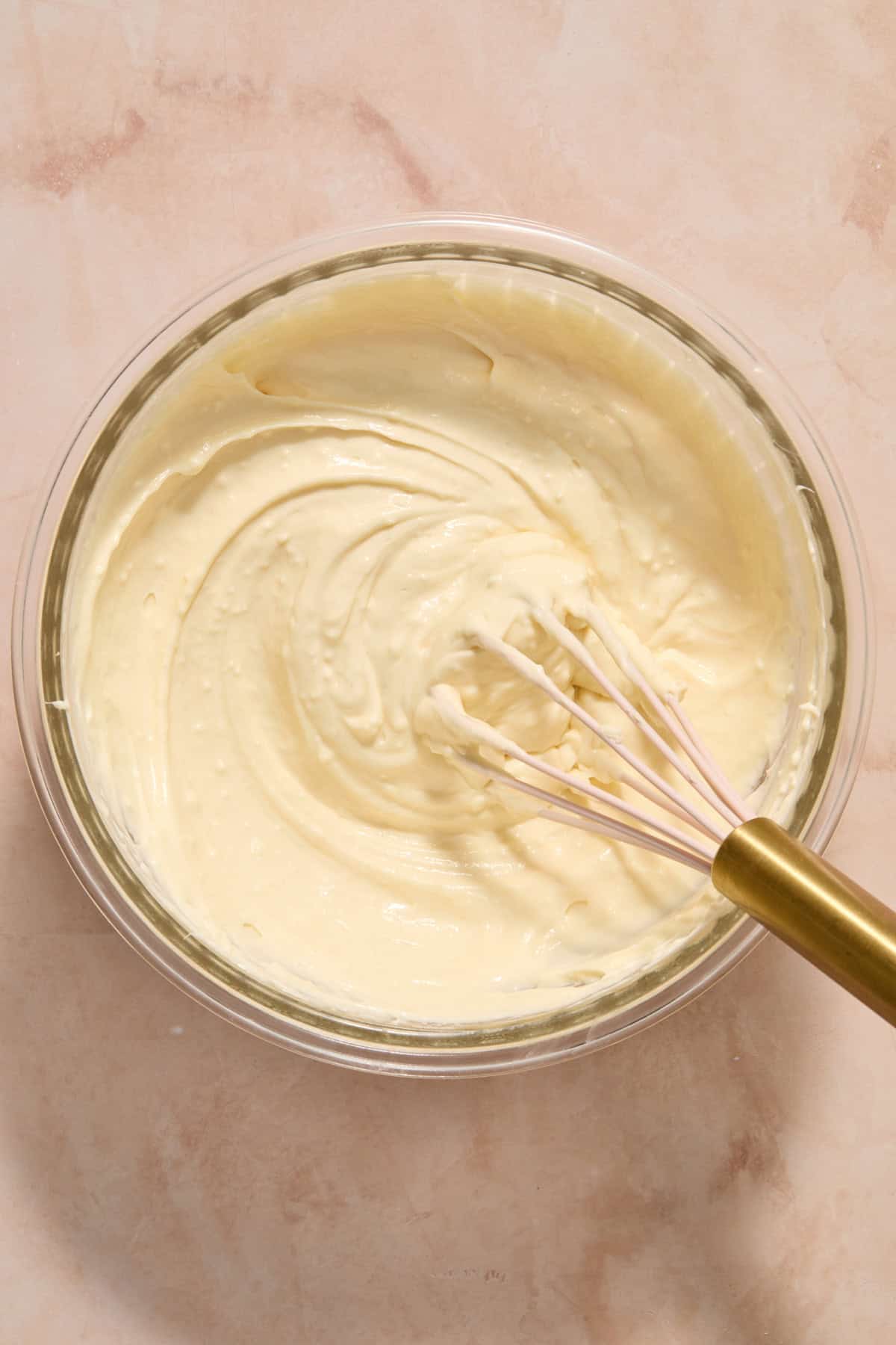 Cheesecake mixture in glass mixing bowl with whisk.