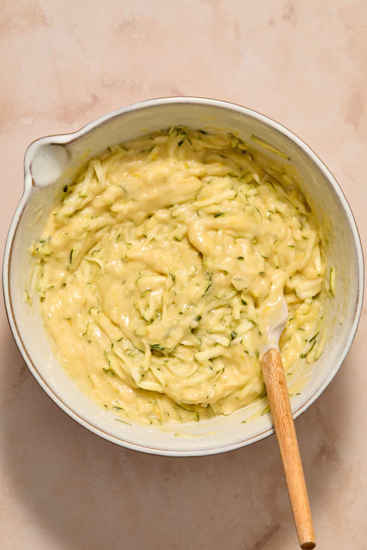 Zucchini folded into batter in bowl with spatula.