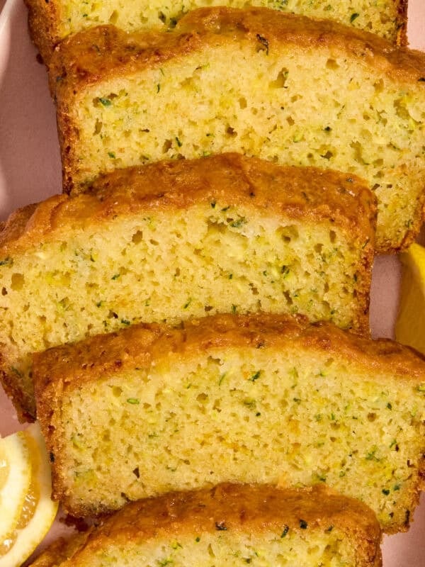 Slices of lemon glazed lemon zucchini bread on plate with lemon wedges.