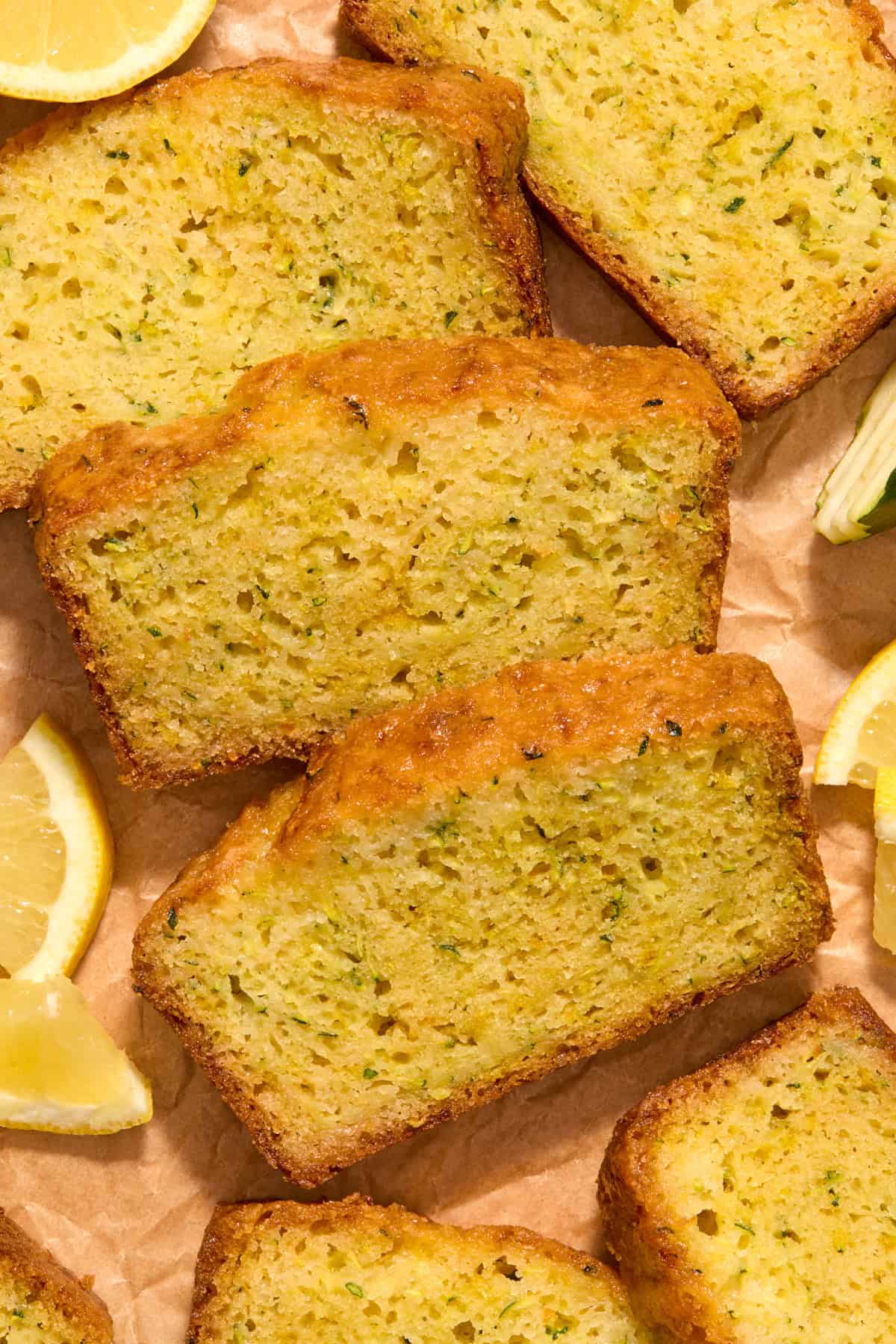 Slices of lemon zucchini bread on parchment with lemon slices.
