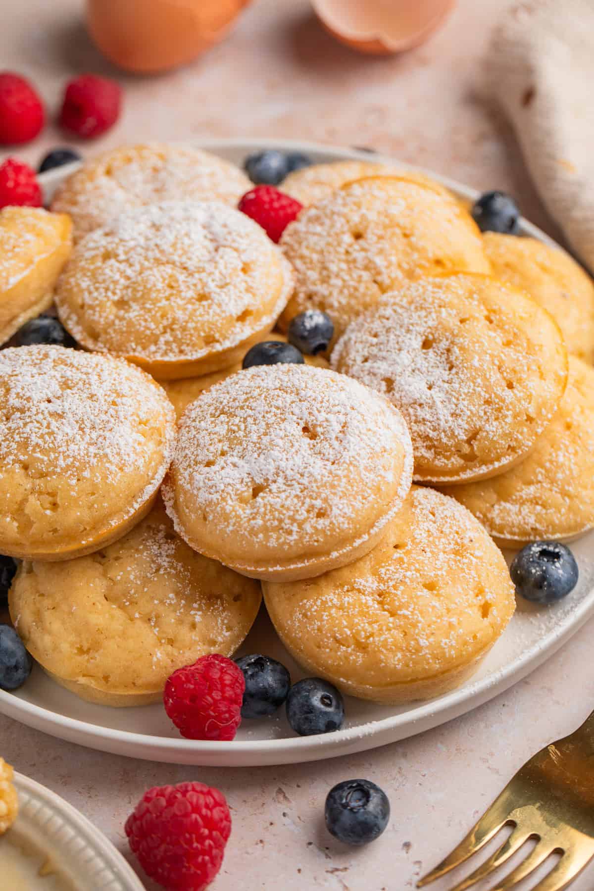 Pancake bites on plate with berries dusted with powdered sugar.
