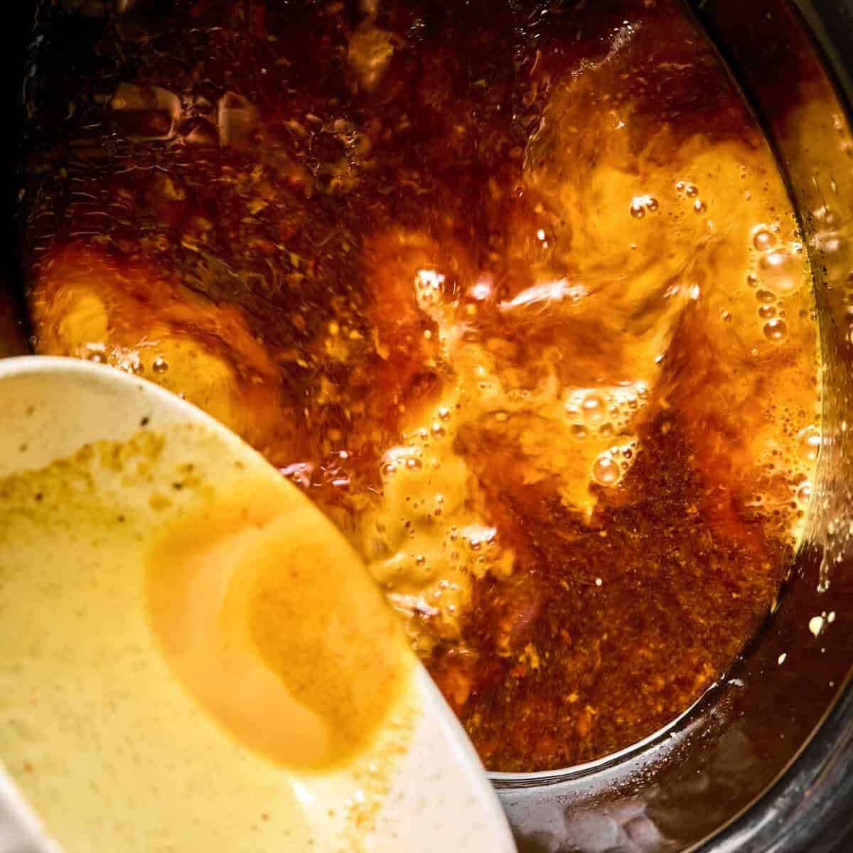 Cornstarch slurry being poured into slow cooker.
