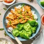 Shredded honey sriracha chicken in sauce over rice with green onions on top.