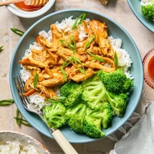 Shredded honey sriracha chicken in sauce over rice with green onions on top.