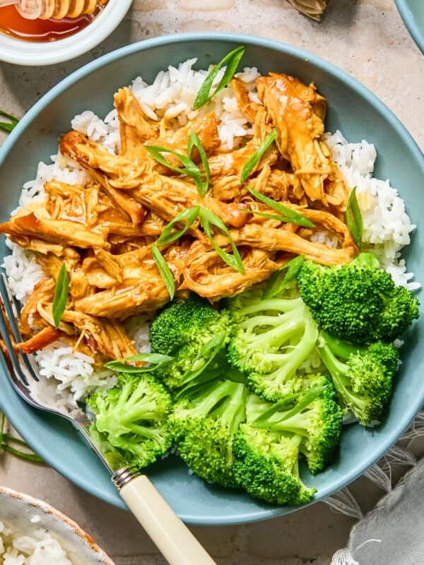 Shredded honey sriracha chicken in sauce over rice with green onions on top.