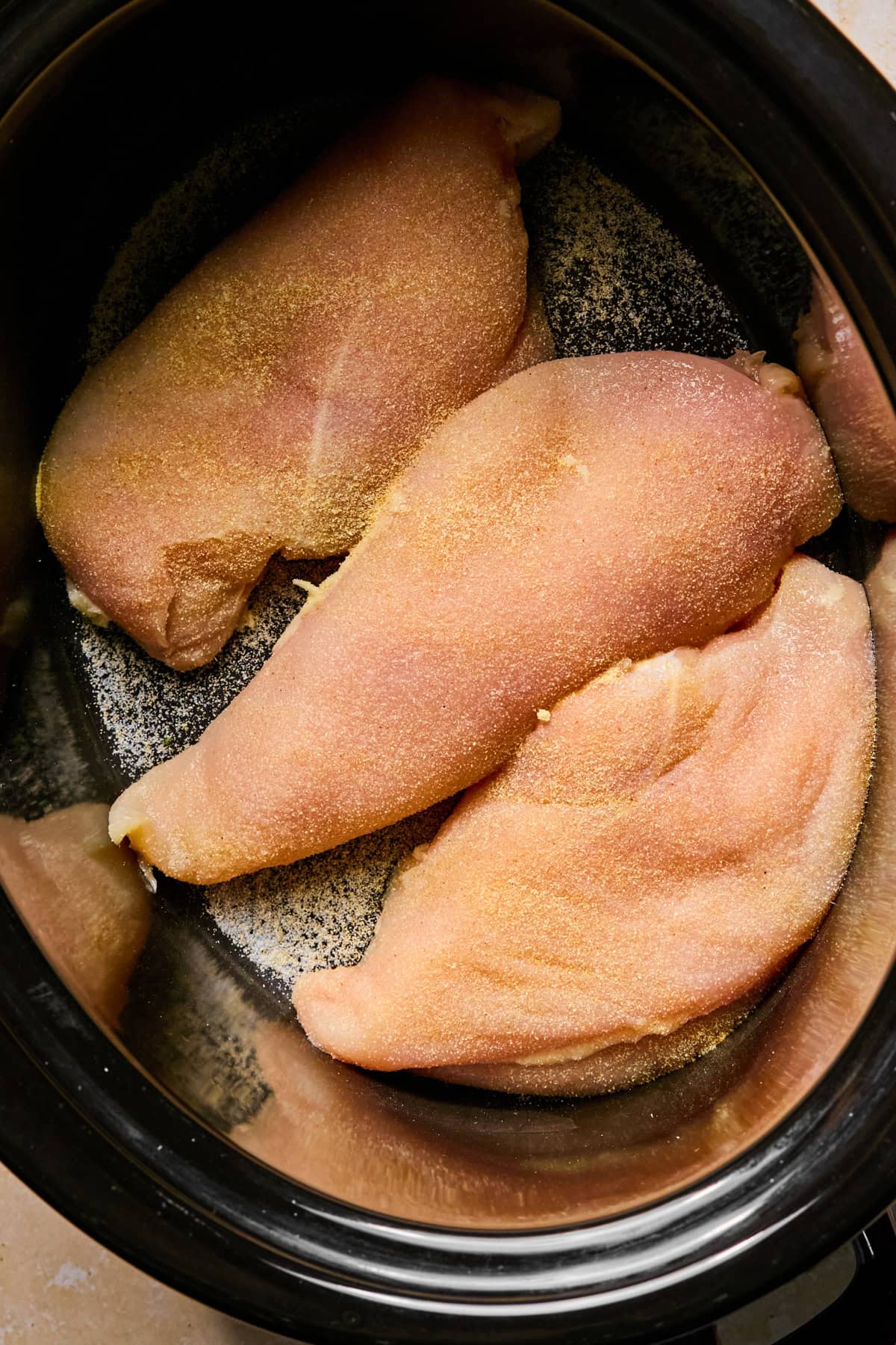 Seasoned chicken breasts in crockpot before cooking.