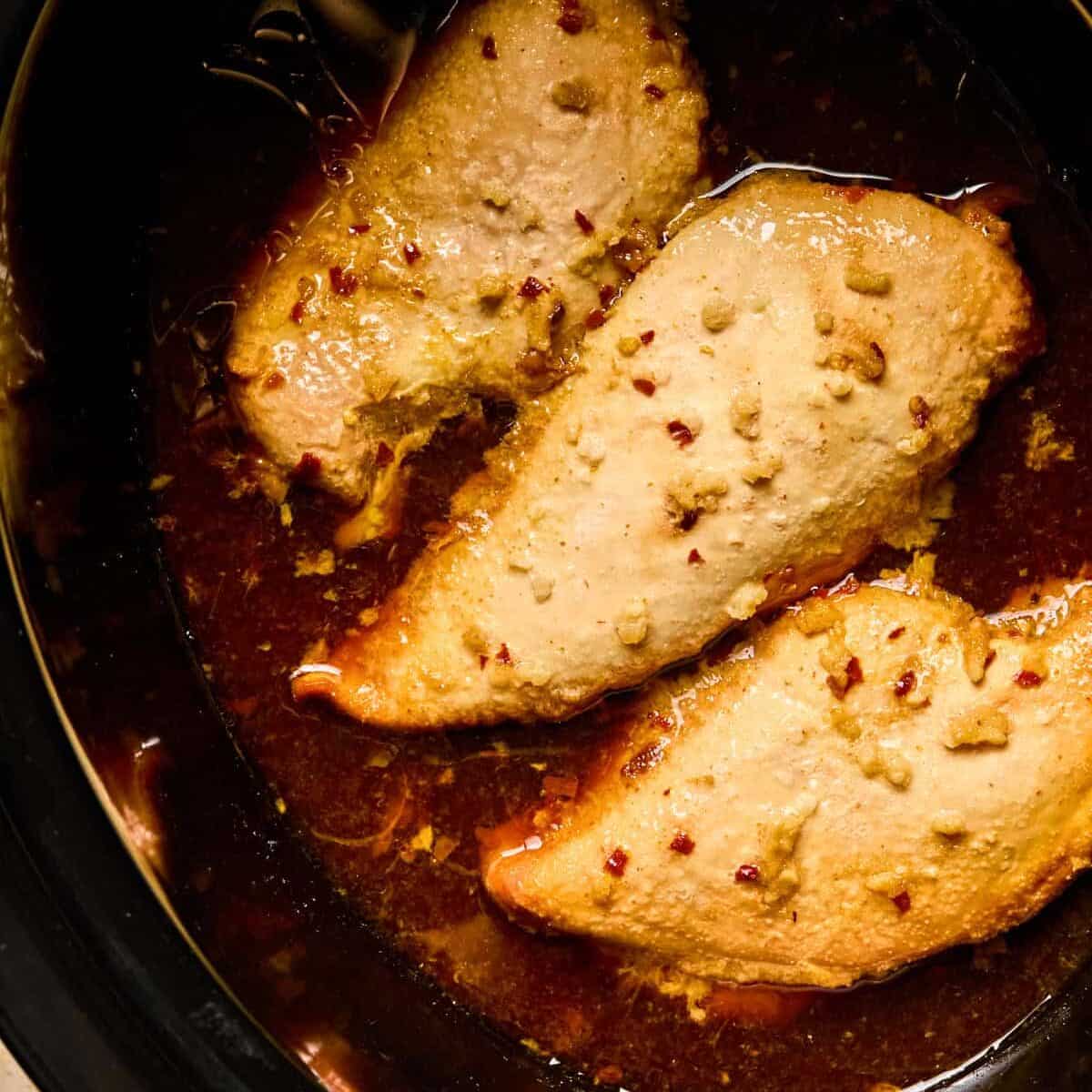 Cooked honey garlic sriracha chicken breasts in crockpot.