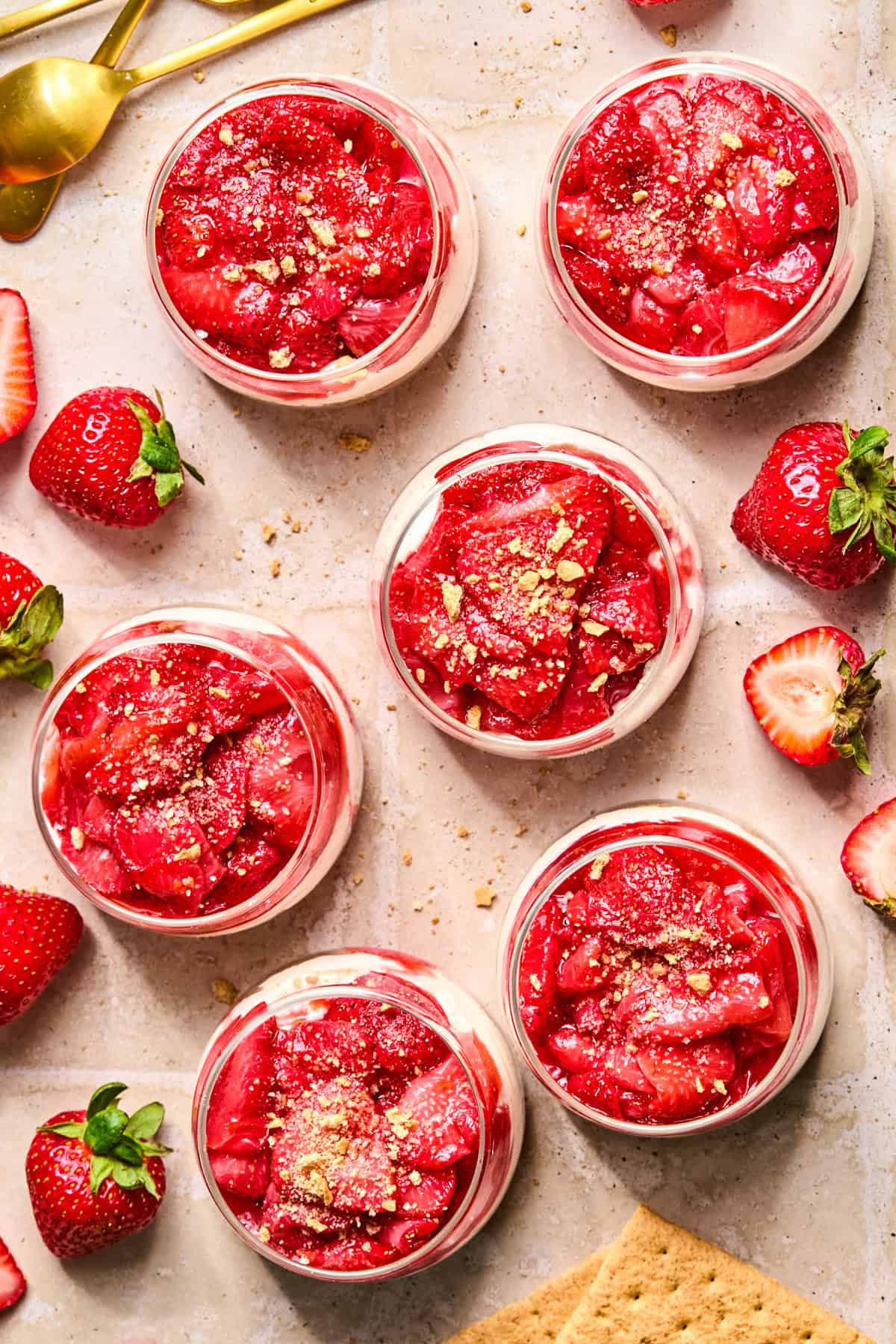 Roasted strawberry cheesecake cups in dessert glasses with graham cracker crumb sprinkle over top.