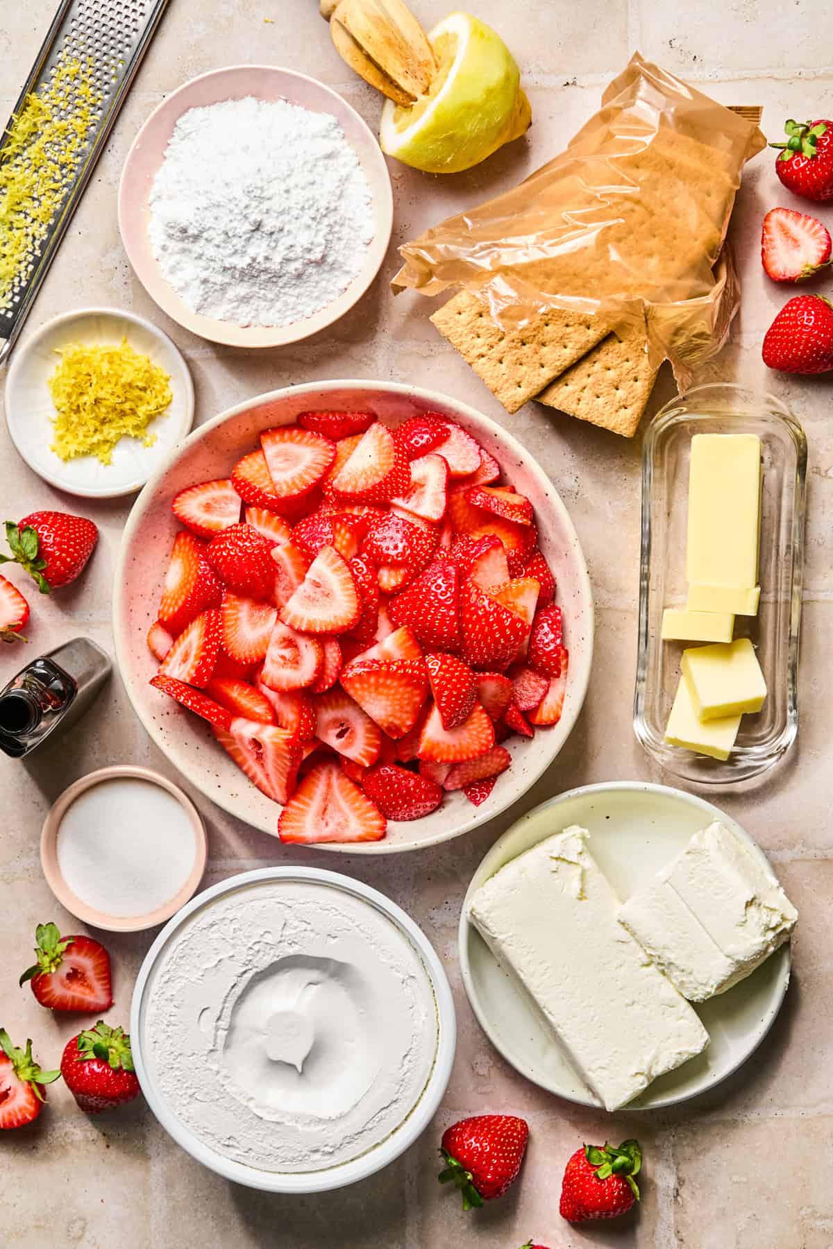 Sliced strawberries, butter, lemons, graham crackers, and other ingredients on surface.