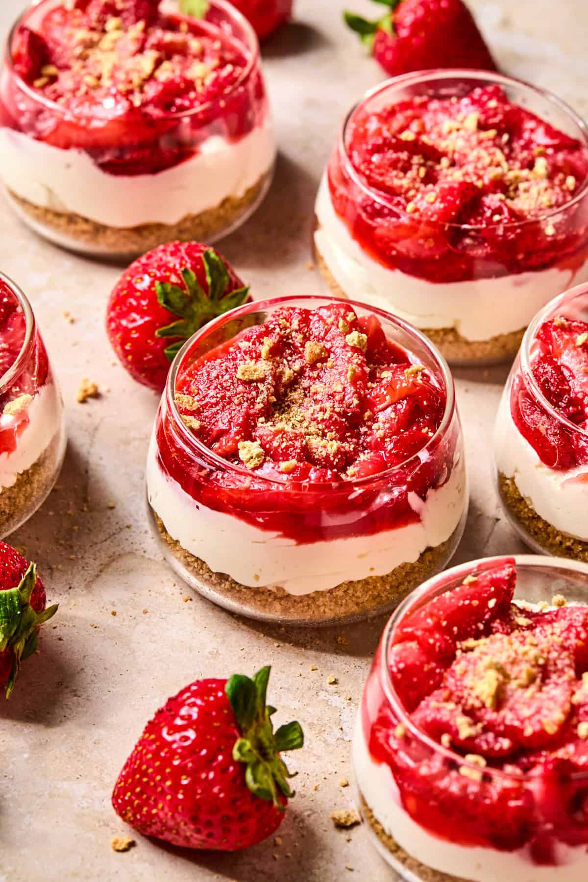Strawberry topped no-bake cheesecake cups with strawberries beside the cups.