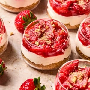 Dessert glass with layered strawberry topped cheesecake cups.
