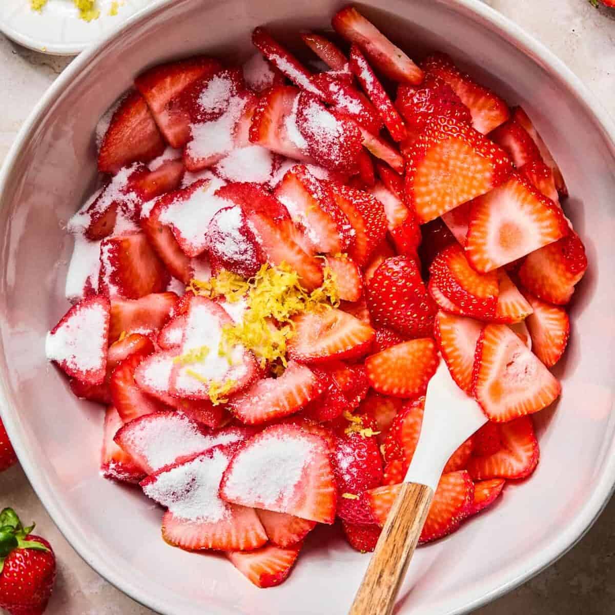 Sliced strawberries in bowl with sugar and lemon zest.