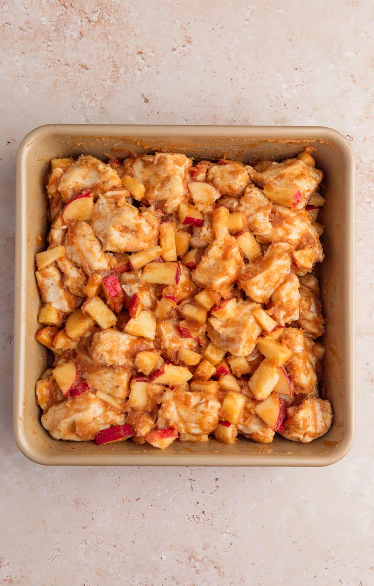 Biscuit dough pieces in baking dish with apples and cinnamon.