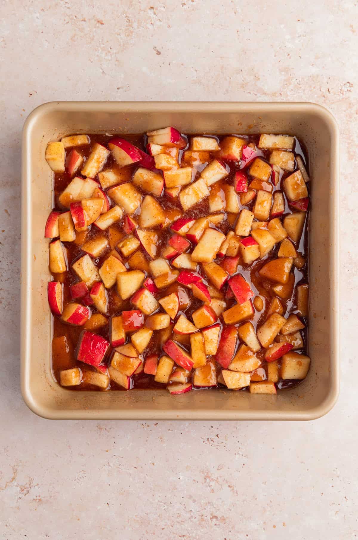 Diced apples added to baking pan with brown sugar and cinnamon mixture.