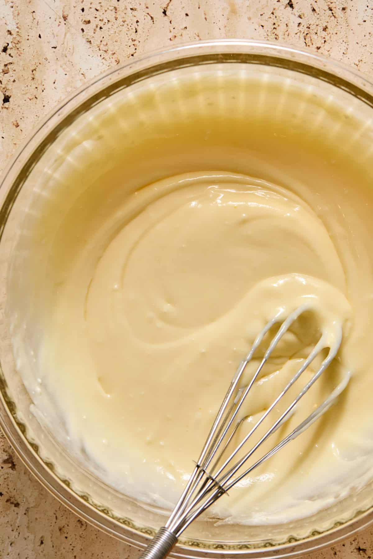 Cheesecake mixture in glass bowl with whisk.