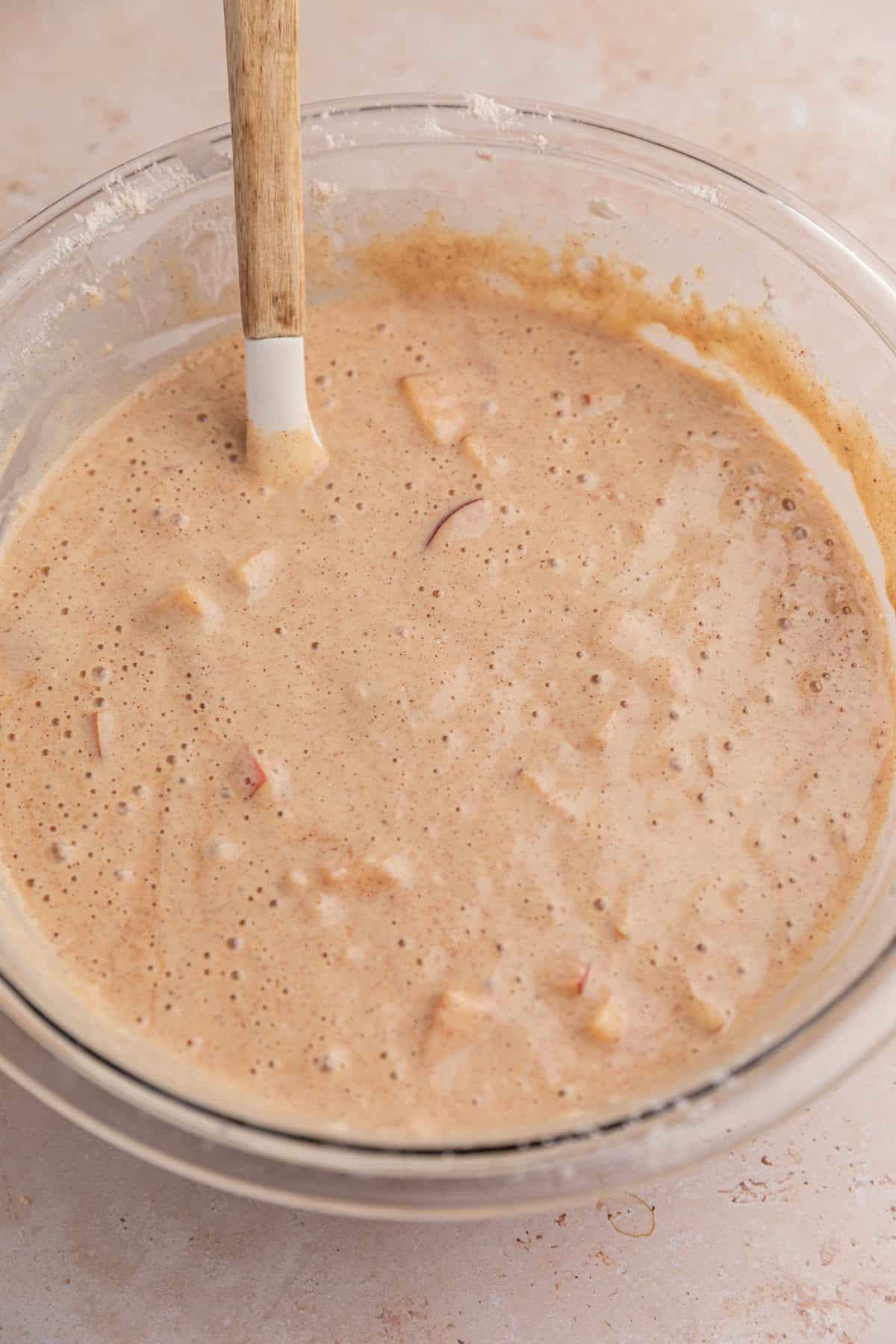 Cinnamon apples added to protein pancake mixture in bowl with spatula.
