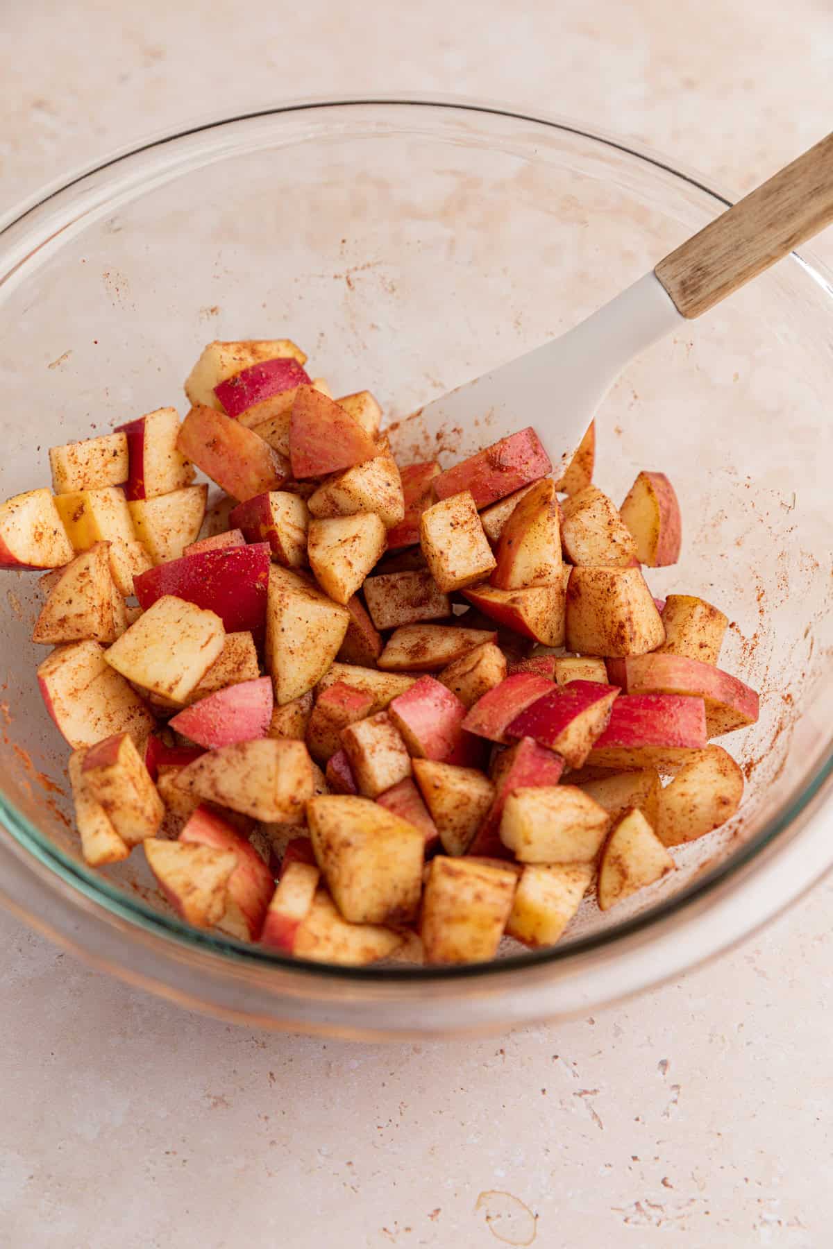 Chopped apples with cinnamon and maple syrup in glass bowl with spatula.