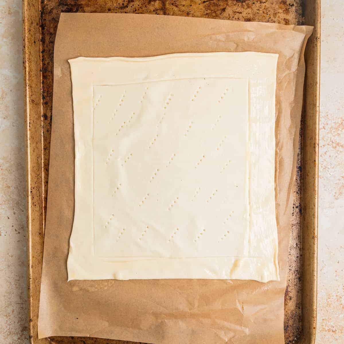 Sheet of puff pastry with edges scored laying on parchment lined sheet pan.