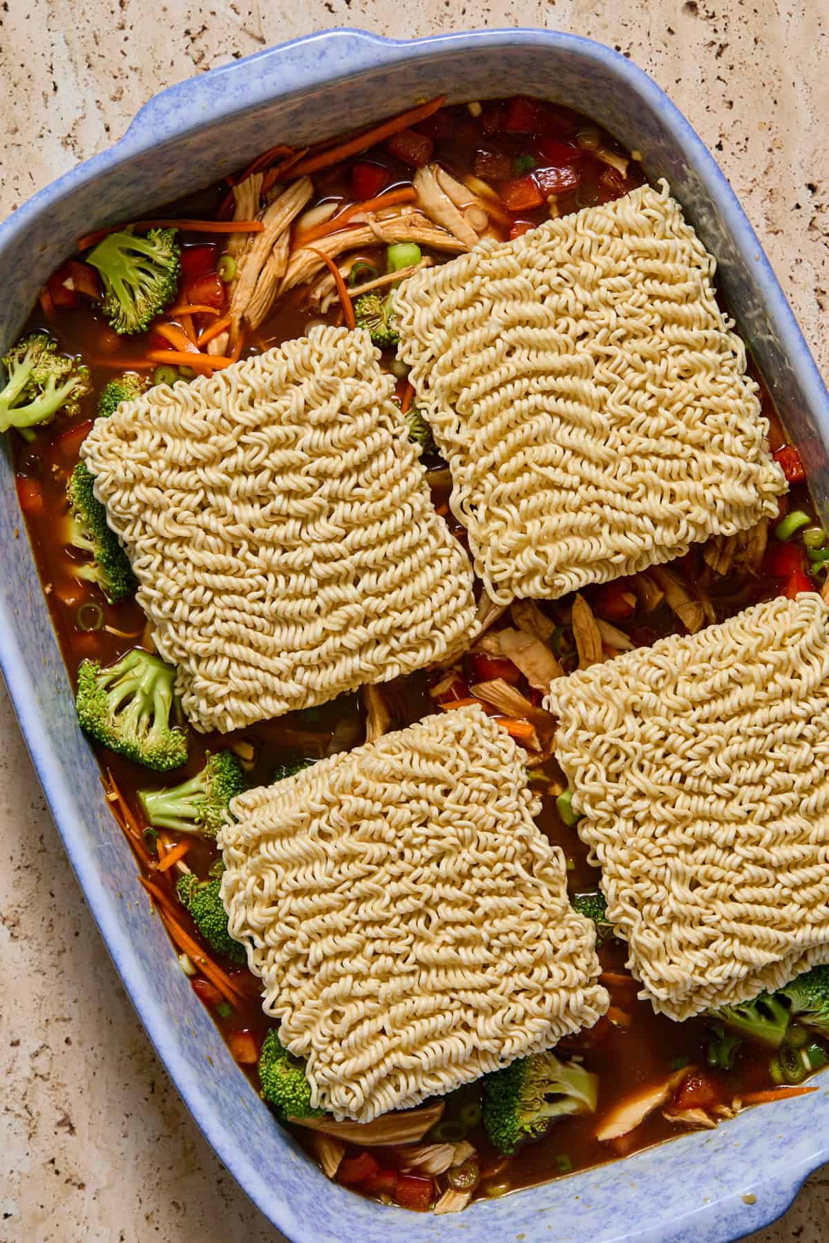 Ramen bricks on top of veggies and sauce in pan before baking.
