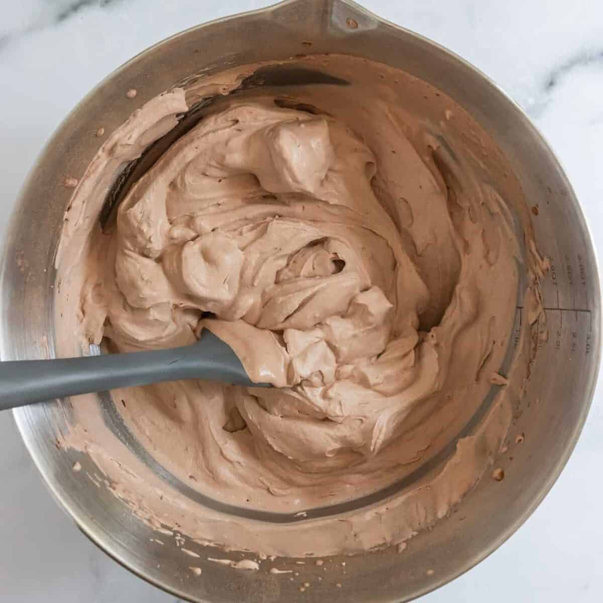 Chocolate whipped cream with stiff peaks in bowl with gray spatula.