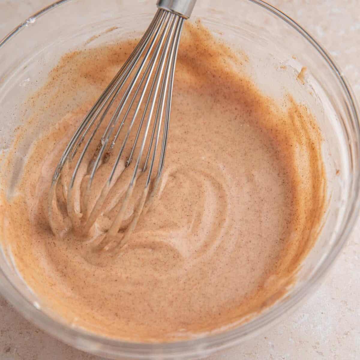 Cinnamon icing in bowl with whisk.