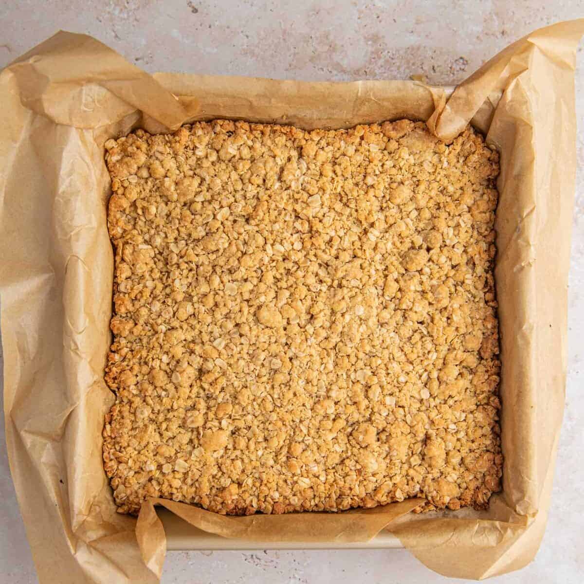 Baked oatmeal cinnamon crumb bars in parchment lined pan.