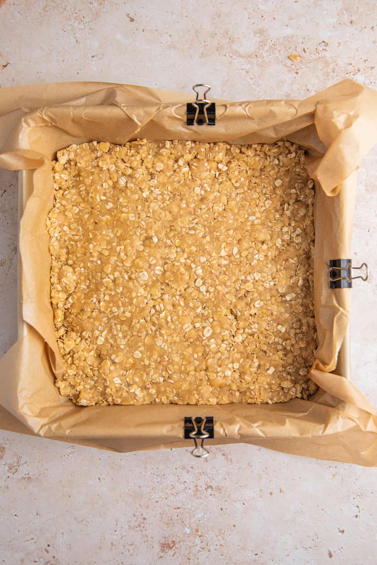 Oat crumb base layer pressed into baking pan lined with parchment.