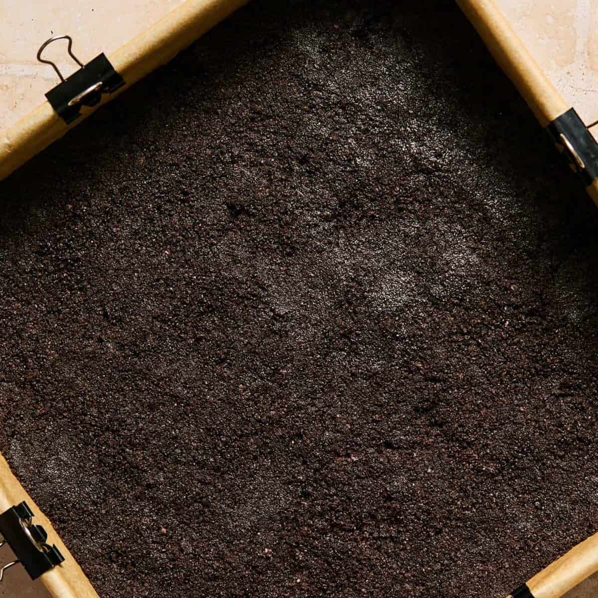 Oreo cookie crust in parchment lined baking pan.
