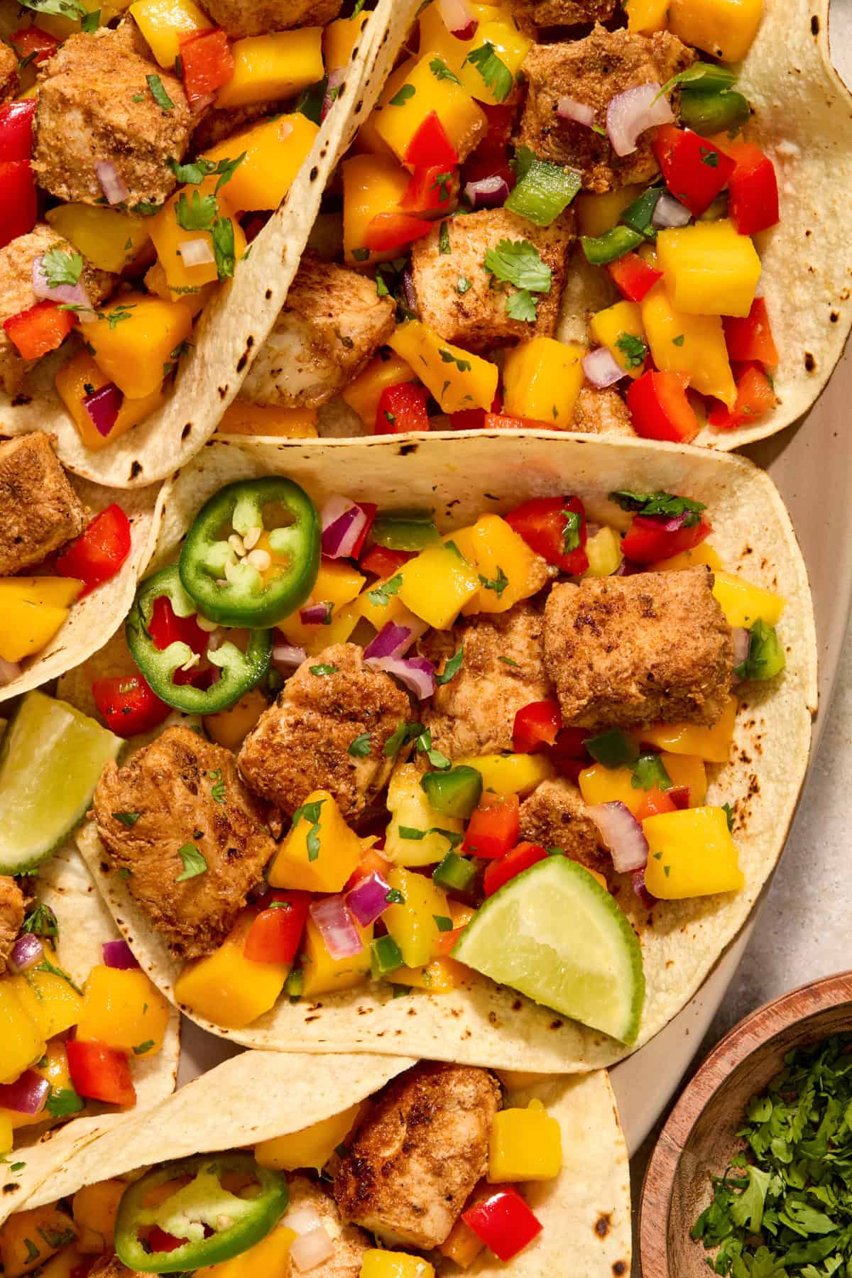 Plate with fish tacos topped with mango salsa and jalapeño slices.