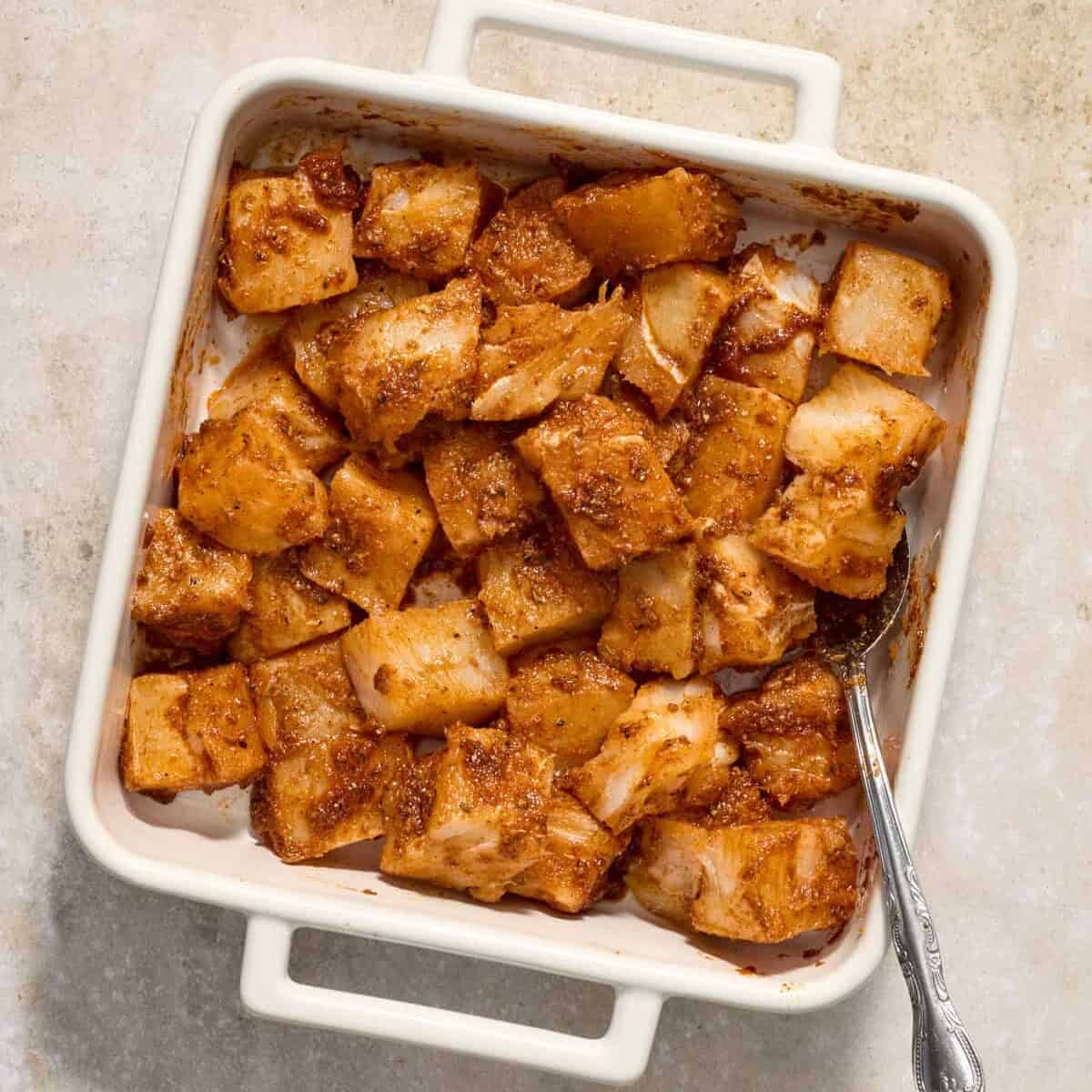 Marinated mahi mahi in glass pan with spoon.