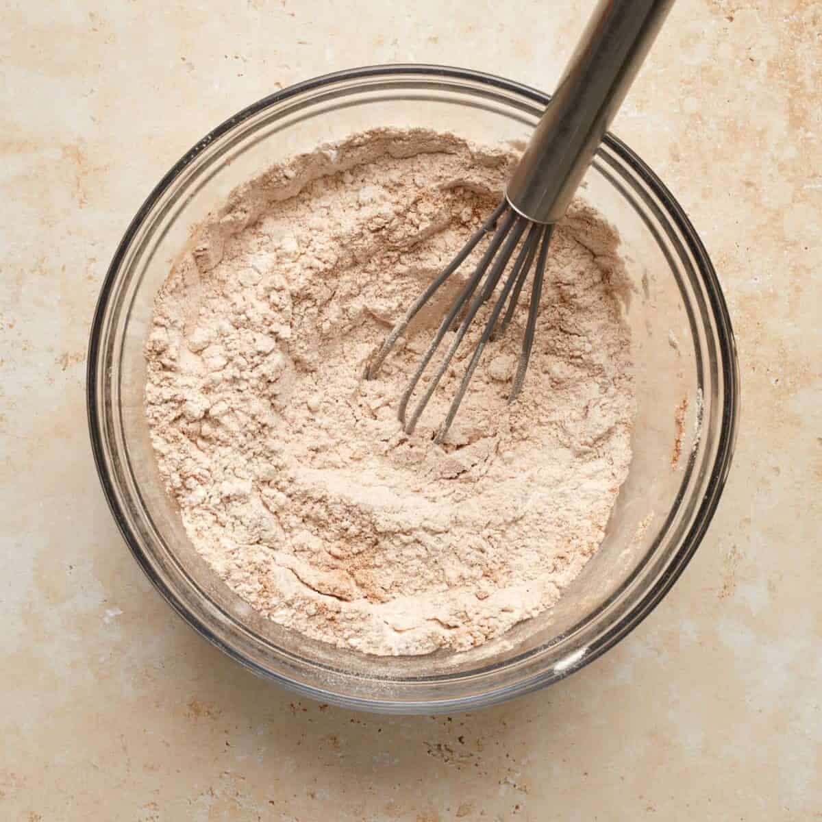 Flour and cinnamon with dry ingredients in bowl with whisk.