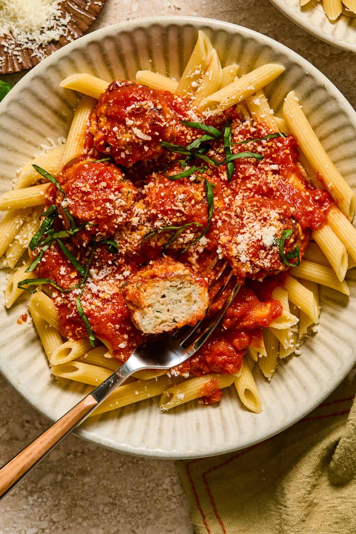 Plate with ricotta chicken meatballs over pasta with fresh parmesan and basil.