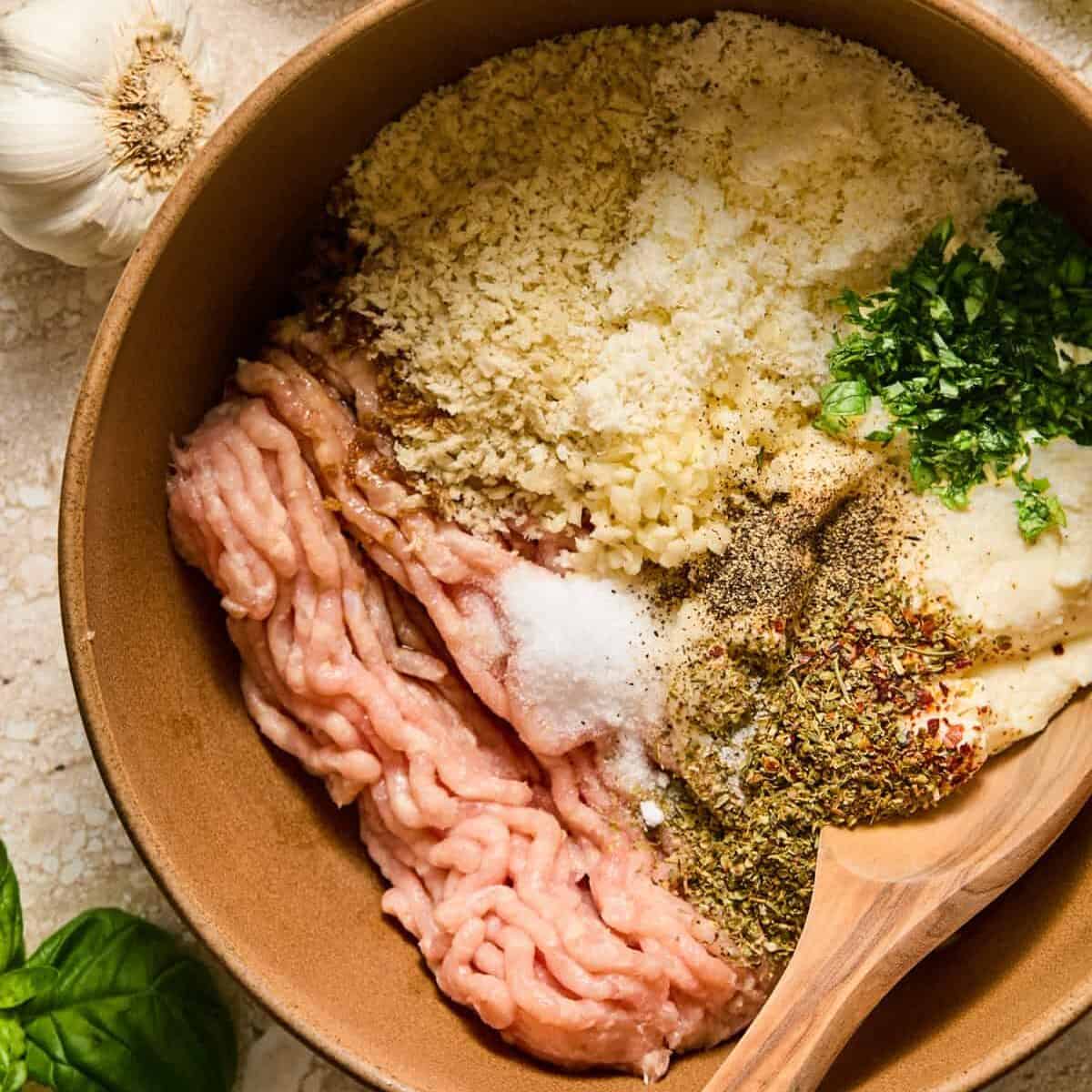 Ground chicken, ricotta cheese, seasoning, parmesan and other ingredients in bowl with wood spoon.