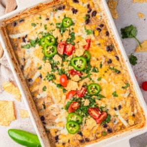 Salsa verde chicken rice bake in pan topped with cilantro, jalapeño and tomatoes.