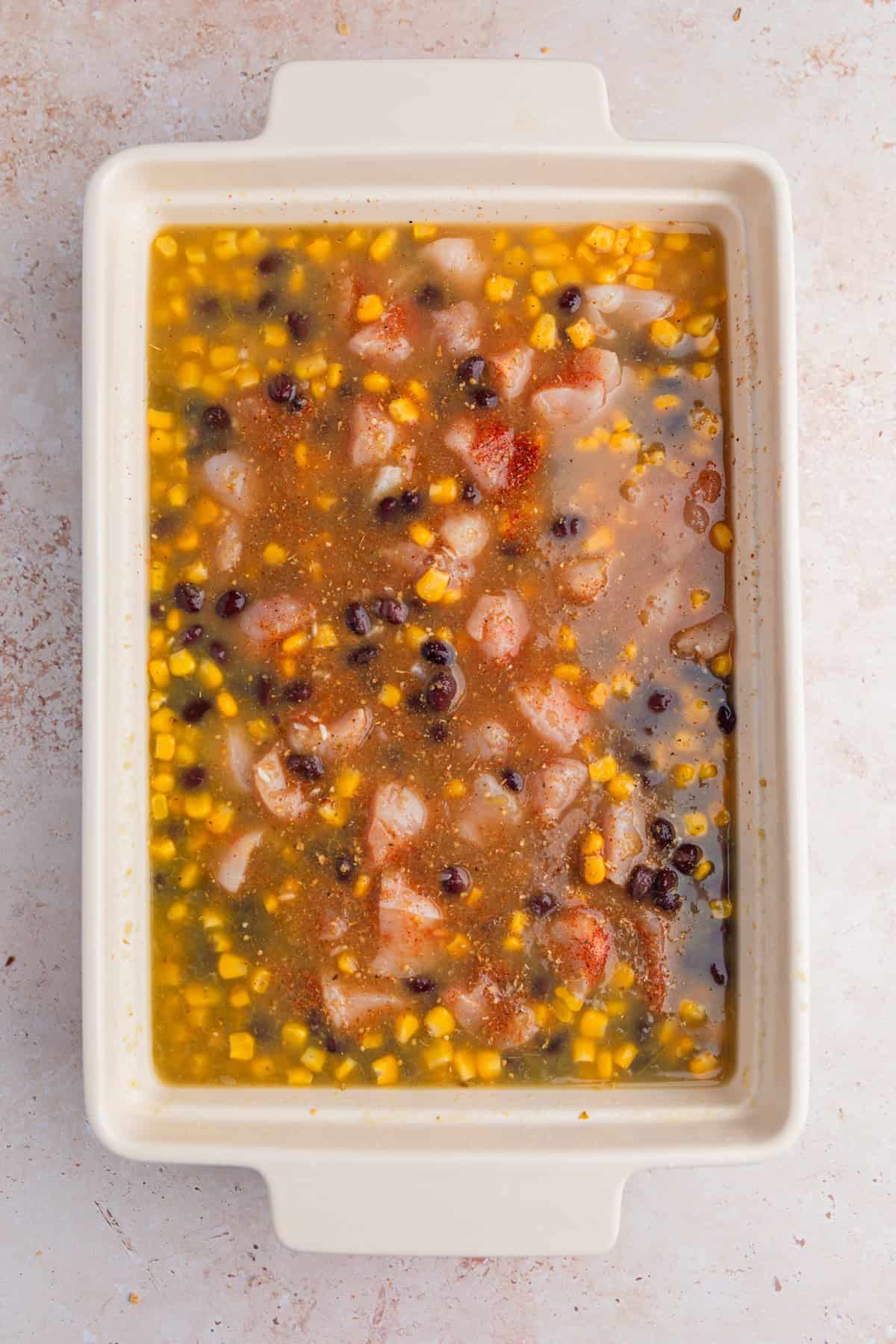 Salsa verde, broth, chicken, corn, beans and seasoning in pan.