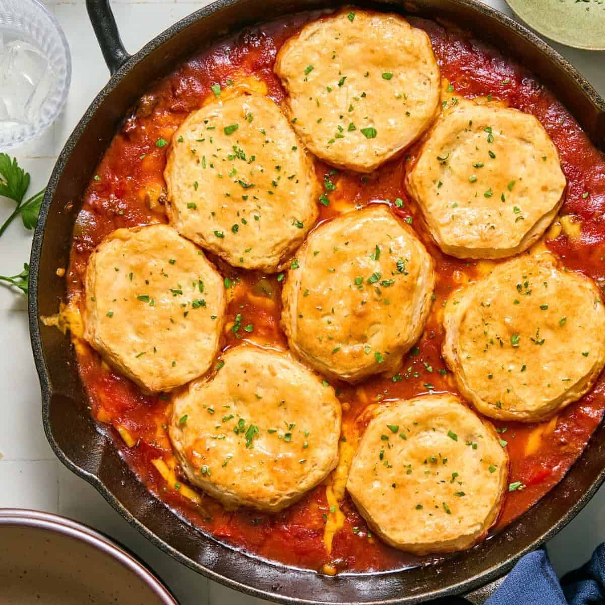 Sloppy Joe casserole prepped in cast iron skillet with parsley topped buttery biscuits.