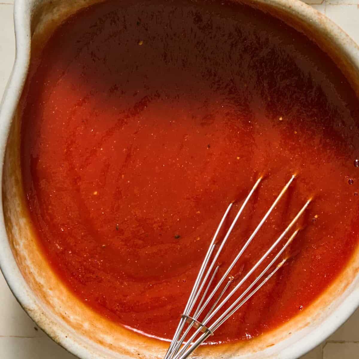 Tomato mixture for sloppy Joe casserole in mixing bowl with whisk.