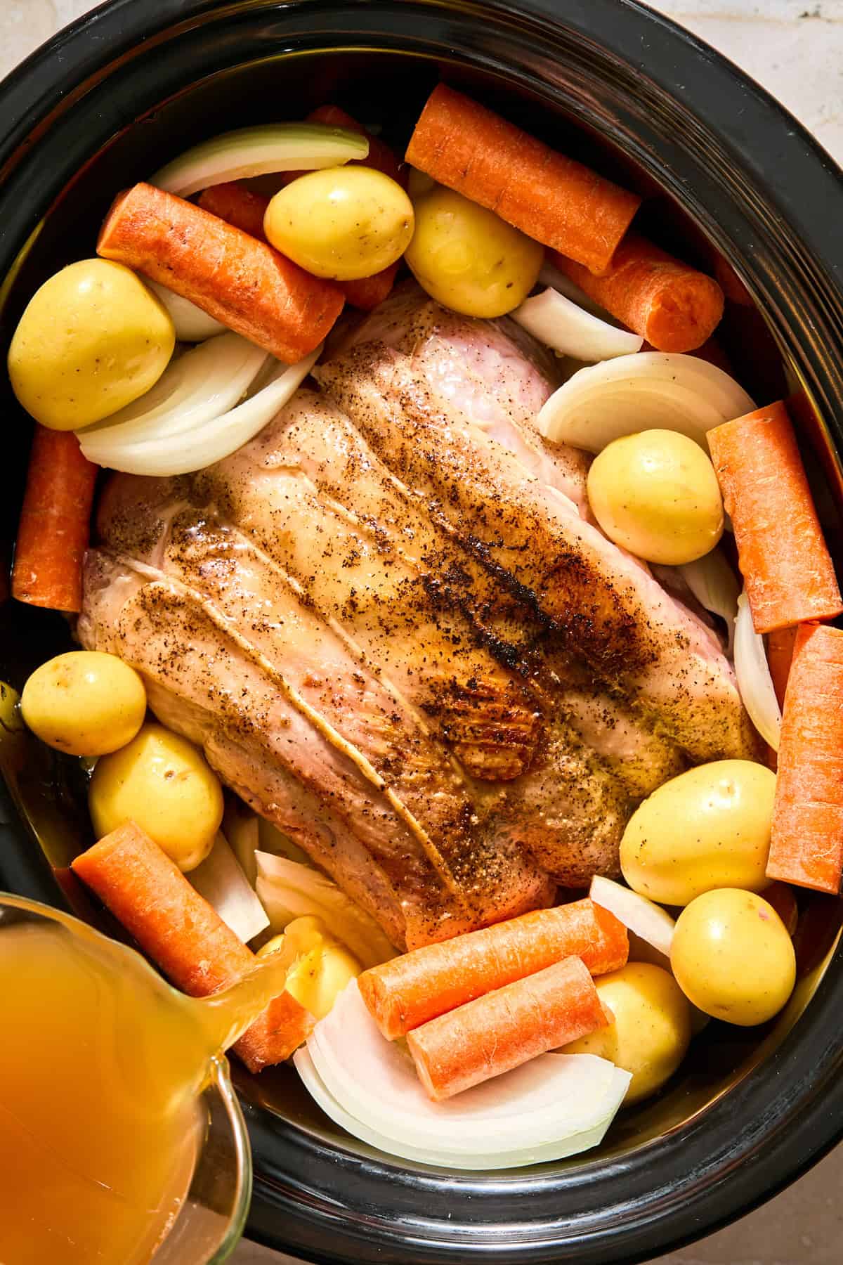 Pork shoulder in crockpot with vegetables surrounding and apple cider mixture poured over top.