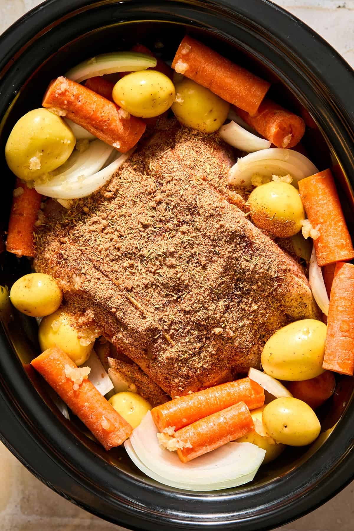 Crockpot with pork topped with pork rub.