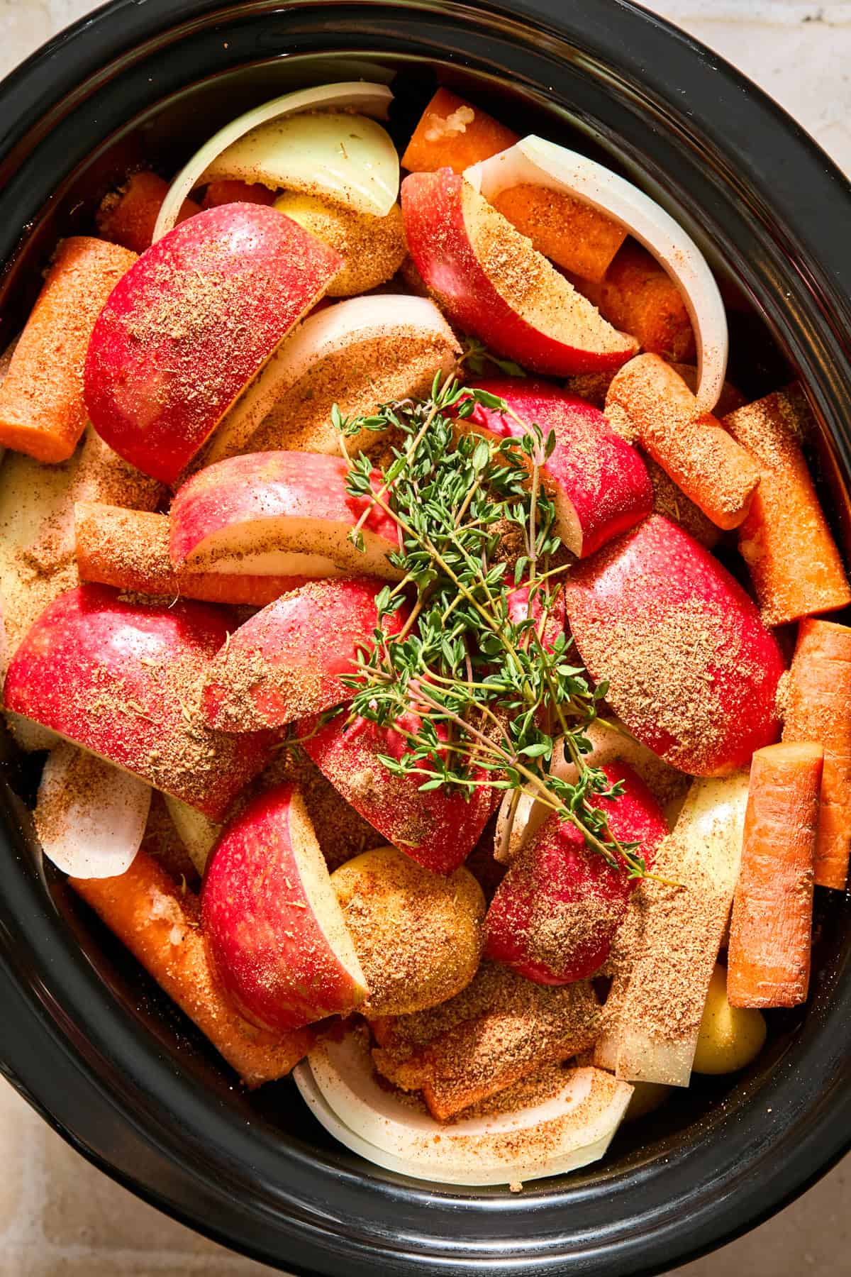 Apples and fresh thyme over top of vegetables and meat in slow cooker.